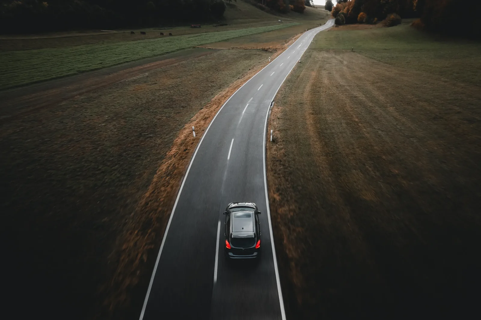 Drohnenaufnahme: Auto in einer weiten Kurve zwischen Feldern — Automobilfotografie Maurice Veith