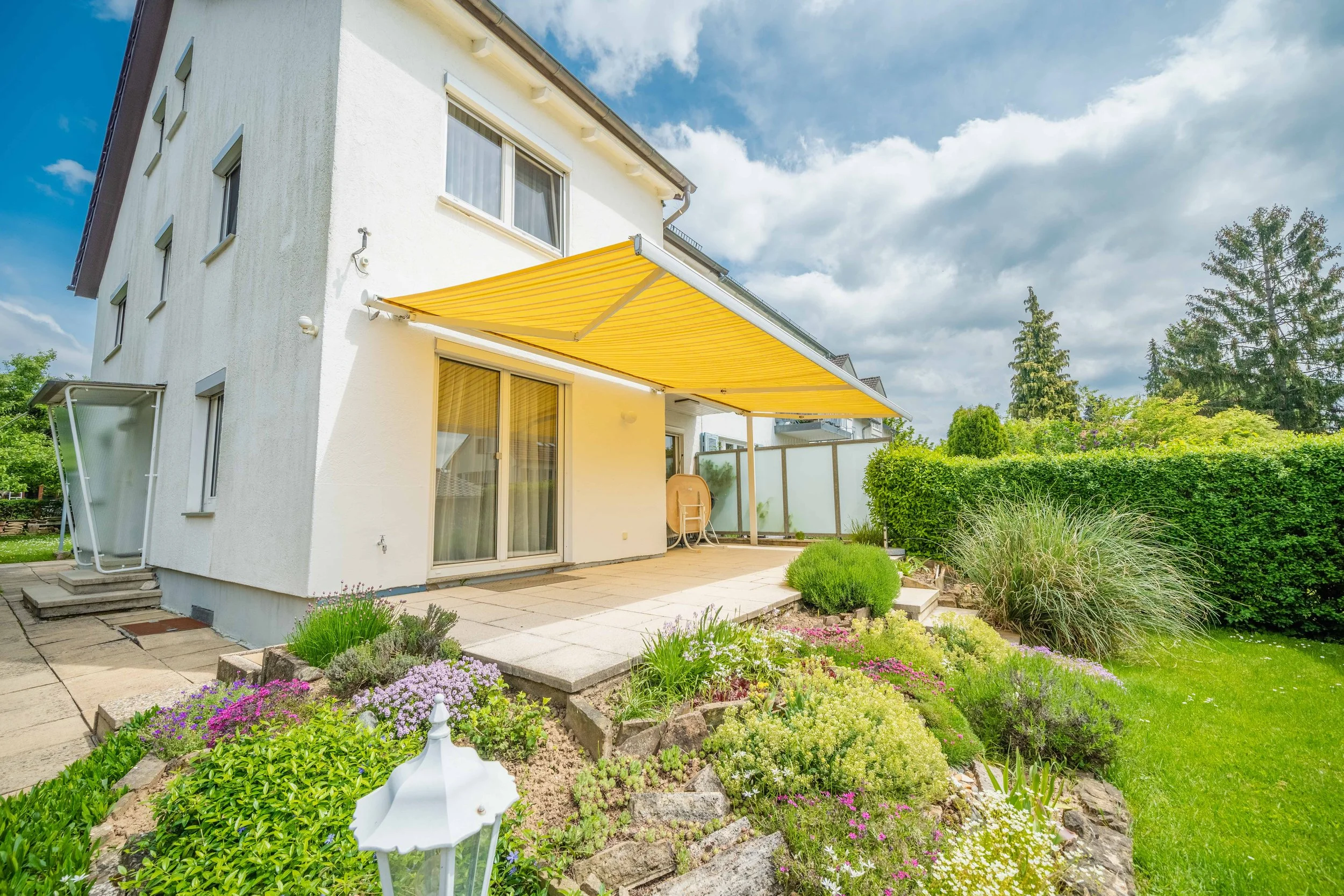 Sonnige Terrasse mit gelber Markise und blühender Gartenanlage — Immobilienfotografie Maurice Veith
